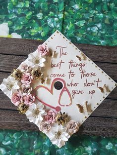 a graduation cap decorated with flowers on top of a wooden table next to a green wall