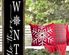 a white bench sitting next to a red pillow on top of a wooden sign with snowflakes