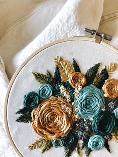 a close up of a embroidery on a white cloth with green and gold flowers in the center