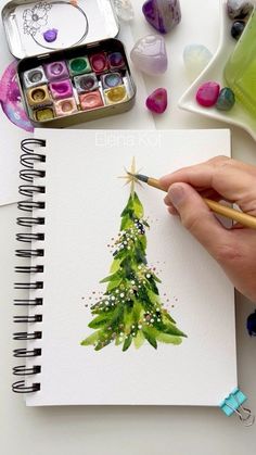 someone is painting a christmas tree on paper with watercolors and paintbrushes