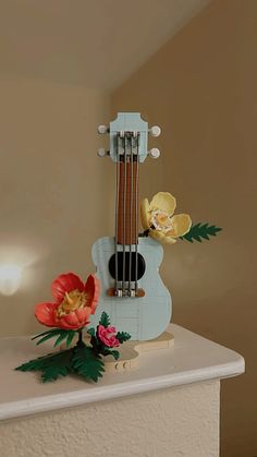 a miniature guitar with flowers on it sitting on top of a counter next to a wall