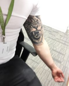 a man with a tiger tattoo on his arm sitting in front of a table and chair