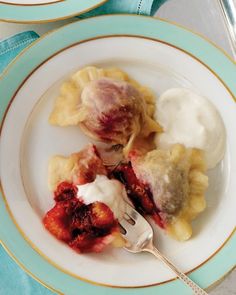 two plates topped with dumplings and fruit on top of a blue table cloth next to silverware