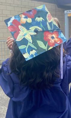 a woman in blue graduation gown holding up a flowered hat with tassels