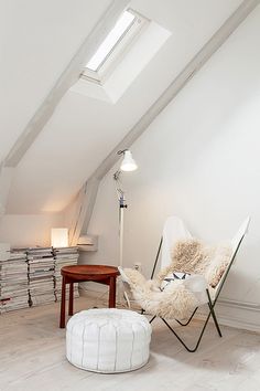 a room with a chair, lamp and books on the floor next to an ottoman