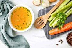 carrots, celery, and other vegetables sit on a towel next to a bowl of soup