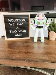 a toy buzz lightyear standing next to a sign that says houston we have two year old