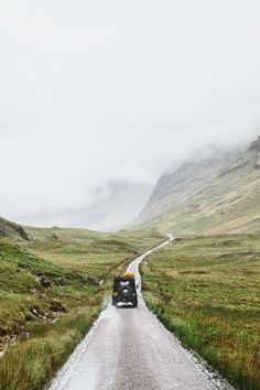 an old car driving down a road in the middle of some grass covered hills and mountains