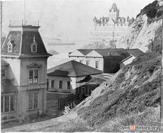 an old black and white photo of some buildings on the side of a hill with water in the background