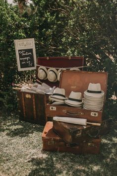 an old suitcase with hats and plates in it sitting on the grass next to trees