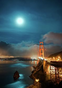 the golden gate bridge is lit up at night with lights on and fog in the air