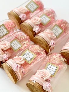 pink and gold wedding favors in glass bottles with tags on them, sitting on a white surface