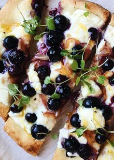 a pizza topped with blueberries and cheese on top of a piece of parchment paper