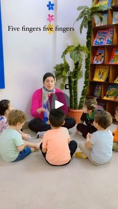 a group of children sitting on the floor in front of a woman talking to them