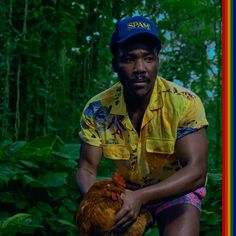 a man kneeling down holding a chicken in front of some trees and bushes with the caption stop