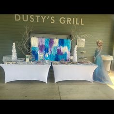 two tables covered in white table cloths and decorated with blue and purple decorations, one is