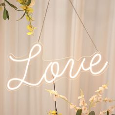 a neon sign that says love hanging from a string with flowers in front of it