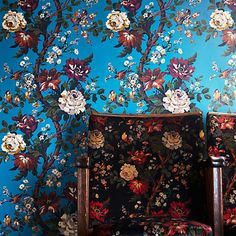 a chair sitting in front of a blue wall with flowers on it and a wooden frame