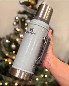 a person holding a stainless steel water bottle in front of a christmas tree