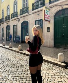 a woman standing in front of a building holding a coffee cup and looking at the camera