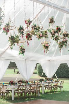 an outdoor wedding setup with white draping and flowers hanging from the ceiling over tables