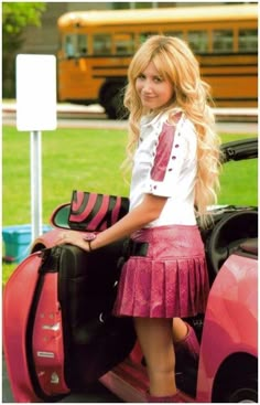 a girl in a pink skirt and white shirt is standing next to a red car