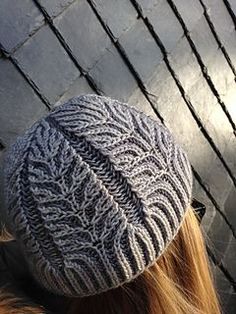 a woman wearing a gray knitted hat next to a wall with black bars on it