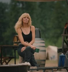 a woman sitting on top of a wooden barrel next to a table filled with barrels