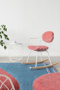 two chairs and a table on a rug in front of a white wall with a potted plant