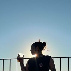 a woman standing next to a fence holding a piece of paper in her hand and looking at the sky