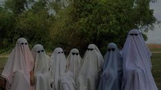 five ghostly people in white and black robes standing next to each other with trees in the background