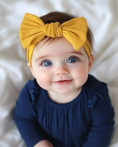 a baby girl wearing a yellow bow on top of her head and smiling at the camera