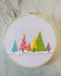 an embroidery project with colorful christmas trees on the front and back of it, sitting on top of a marble surface