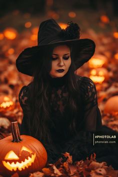 a woman in a black dress and hat sitting on the ground with pumpkins around her