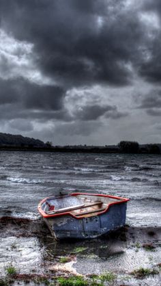 a boat sitting on top of a sandy beach under a cloudy sky with dark clouds