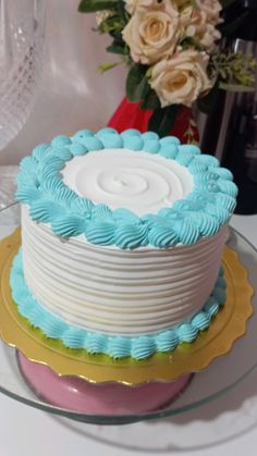 a white and blue cake sitting on top of a table next to a vase filled with flowers