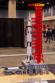 a lego model of a rocket on display at an exhibit in a building with people standing around it