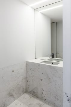 a white bathroom with marble counter top and mirror above the sink in front of it