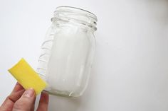 a hand holding a sponge next to a mason jar