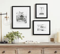 three framed photographs hang on the wall above a dresser with a vase and glasses next to it