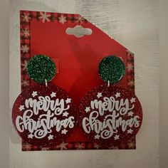 red and white earrings with merry christmas written on them in front of a red card