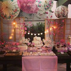 a table topped with lots of cakes and desserts covered in pink paper umbrellas