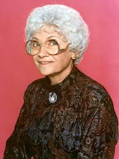 an older woman wearing glasses and a black dress with floral designs on it's sleeves