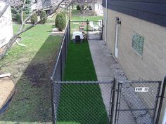 a fenced in yard with artificial grass on the ground and a dog house behind it