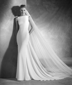 a woman in a wedding dress standing next to a wall with her veil pulled back