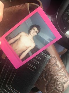 a person holding up a pink polaroid with a shirtless man's image on it