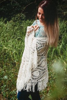 a woman standing in the grass wearing a white crocheted shawl with fringes