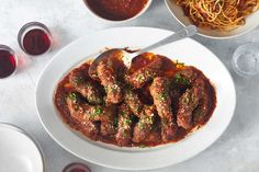 a white plate topped with meat covered in sauce next to bowls of spaghetti and wine glasses