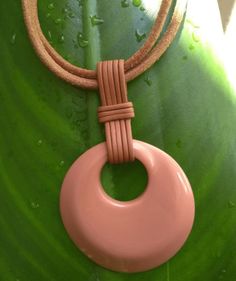 a pink necklace on a green leaf with water droplets around it and a brown cord