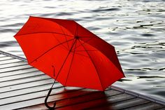 an open red umbrella sitting on top of a wooden dock next to the water,